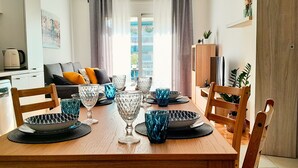 A dining area with a wooden table set for four, surrounded by chairs, with a kitchen in the background. - GPK Lux 2BR | 7 min walking to Acropolis (Athina)