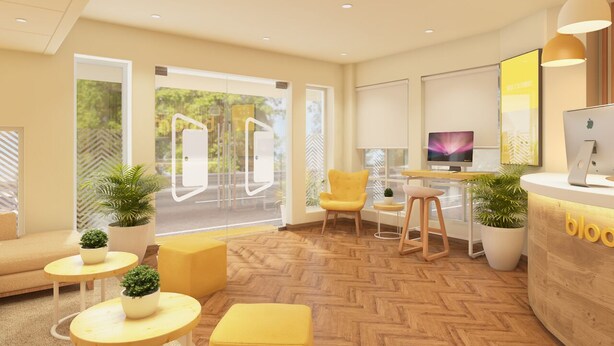 Et moderne receptionsområde med en gulvbelagt parketgulv, gul siddemøbler og en receptionsdisk med en computer og en plante.