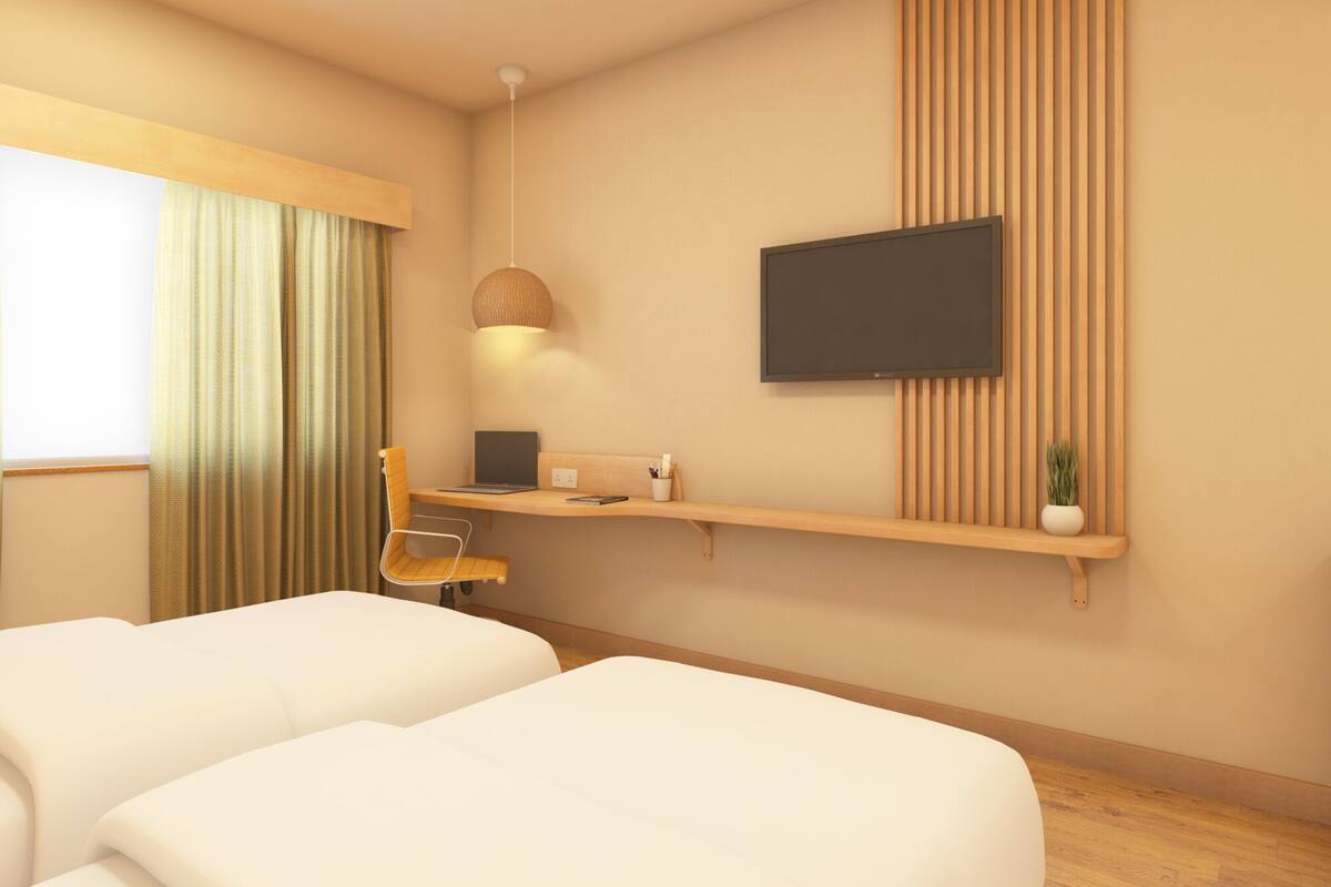 A modern hotel room with a bed, a desk with a laptop, a TV mounted on the wall, and a window with curtains.