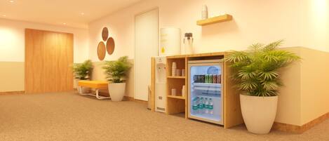 Un área de recepción con un mostrador de madera, una zona de estar, un dispensador de agua y un refrigerador lleno de bebidas.