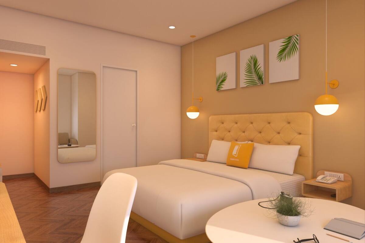A modern hotel room with a large bed, a round dining table, a small side table, a mirror, and wall-mounted artwork.