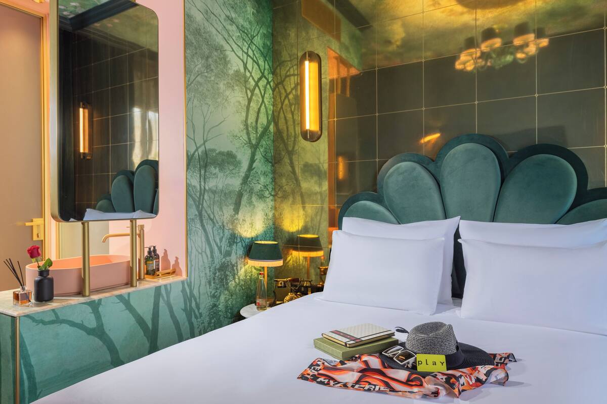 Quarto de hotel moderno com uma cama grande, uma toucador com espelho e uma parede de mármore verde.