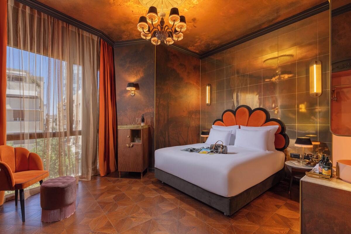 Quarto de hotel com uma cama grande, uma escrivaninha, uma cadeira, uma mesinha e vista para o exterior.
