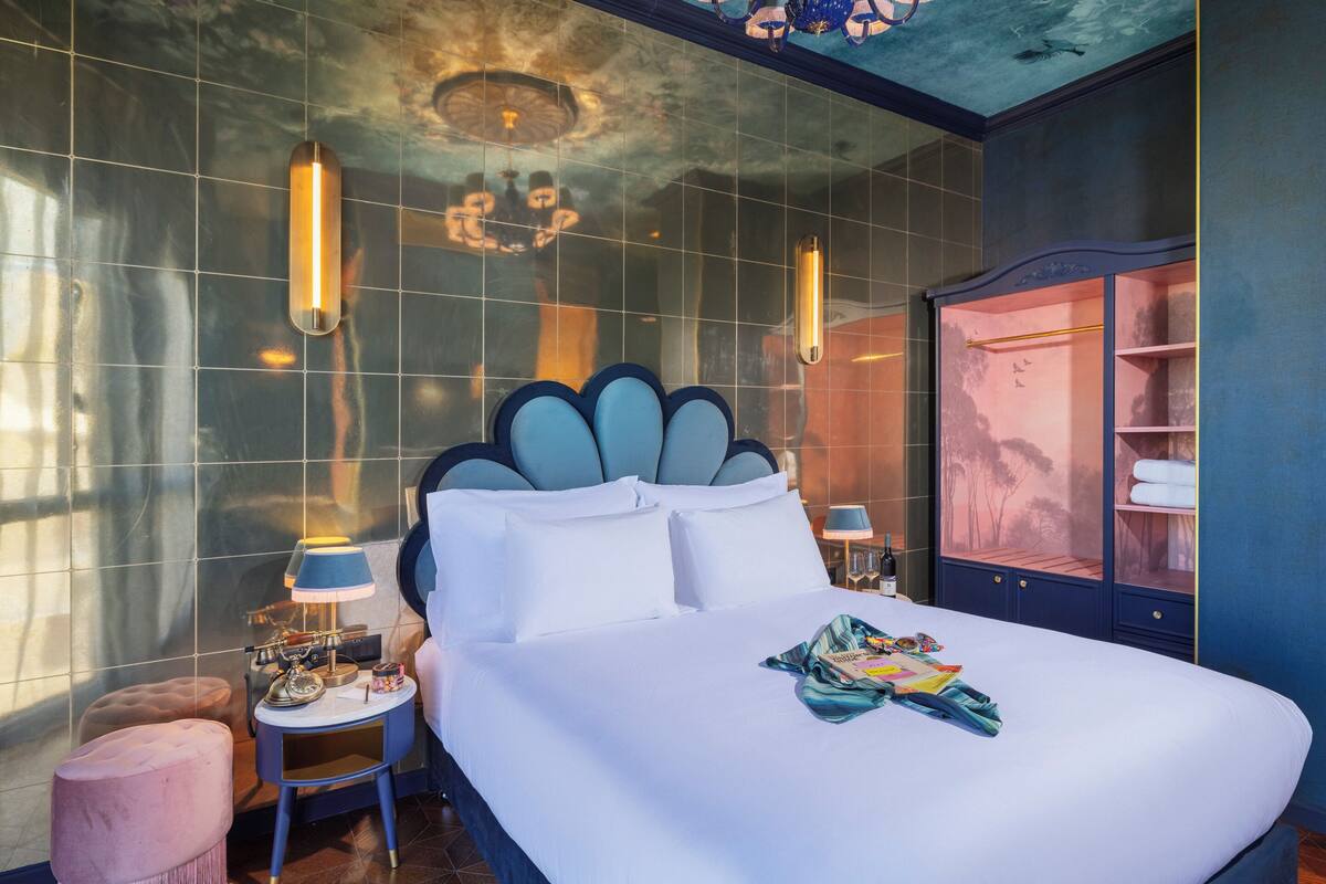 Quarto de hotel moderno com uma cama grande, uma mesa de toucador com espelho e um guarda-roupa com porta de vidro.