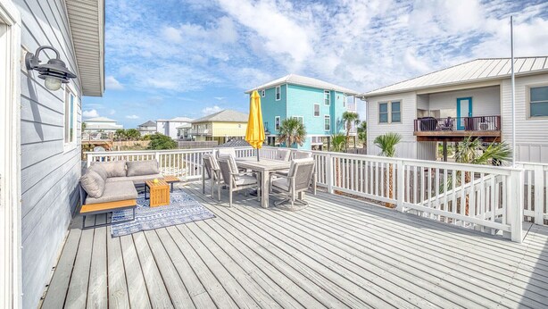 A wooden deck with a sofa and table, a yellow umbrella, and a blue building in the background.