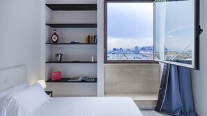 A hotel room with a bed, a bookshelf, a window with a view of a cityscape, and a curtain. - Chic Modern Lofts by Wonderful Italy (Genoa)
