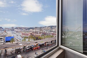 Un paisaje urbano con un puerto deportivo, una concurrida calle con autobuses y automóviles, y un cielo despejado.