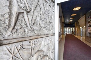 Un pasillo con un detallado relieve de piedra en la pared y un piso cubierto de alfombra roja.