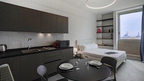 A modern hotel room with a kitchenette, a dining area, and a large window with a view of the city. - Chic Modern Lofts by Wonderful Italy (Genoa)