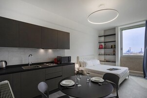 Una habitación de hotel moderna con kitchenette, zona de comedor y un ventanal con vistas a la ciudad.