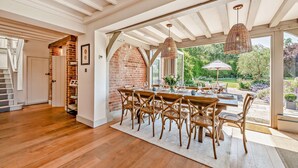 A dining area with a brick wall, wooden ceiling beams, and a view of the garden.
