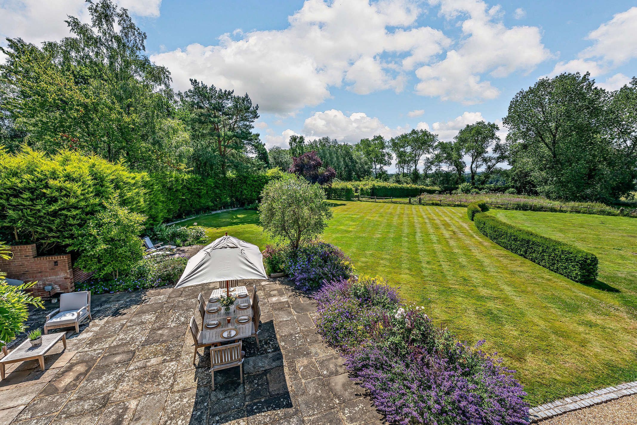 A patio area with a table and chairs, surrounded by lush greenery and a well-manicured lawn.