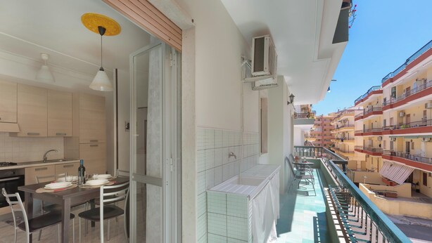 Een balkon met uitzicht op een rij gebouwen, een zithoek met een tafel en stoelen, en een airconditioner aan de muur bevestigd.