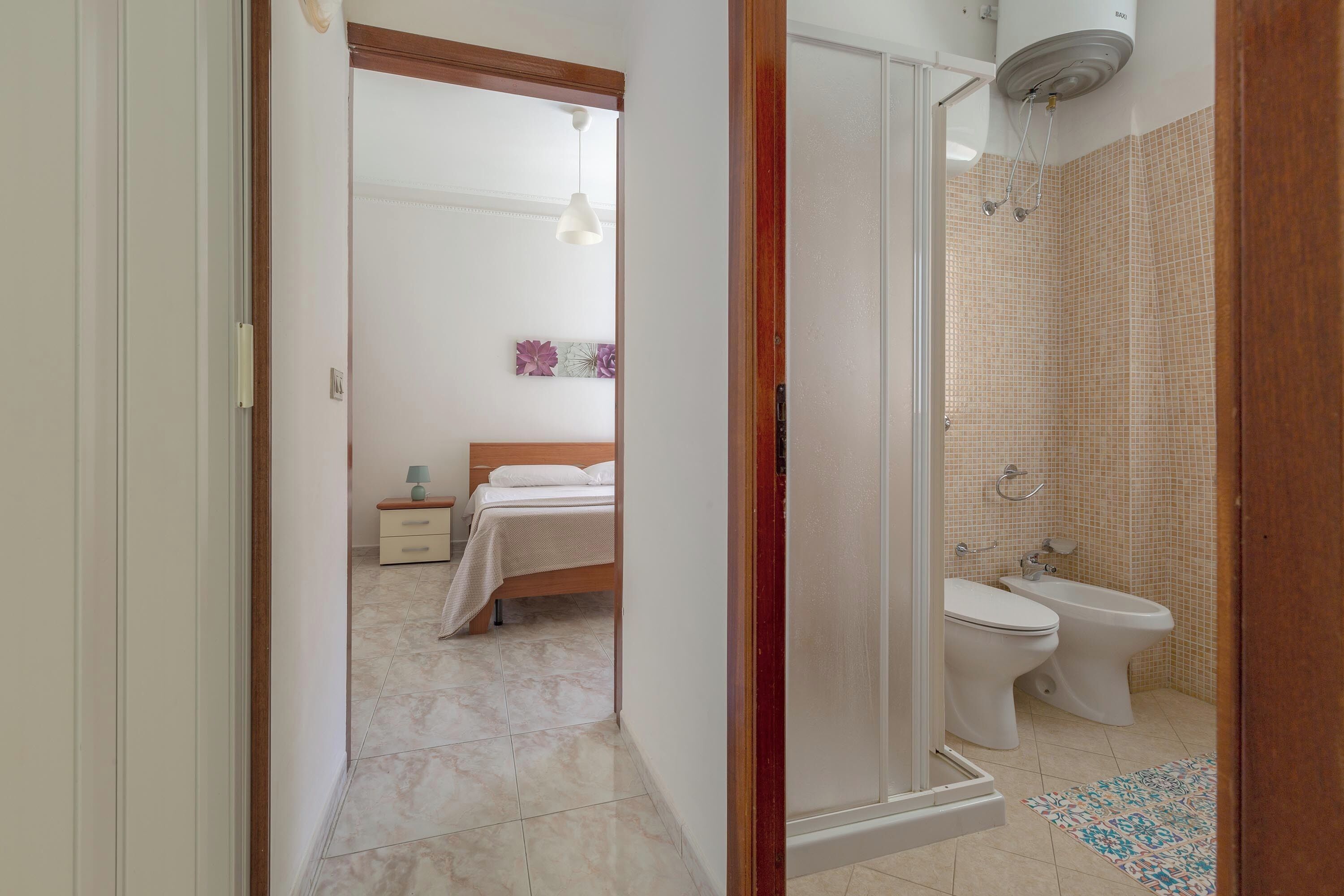 A bathroom with a shower, toilet, bidet, and a small rug.