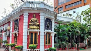 Un edificio con una estatua central de una figura sentada, rodeado por una fachada roja y blanca con detalles decorativos.