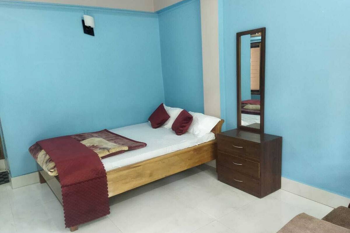 A bedroom with a single bed, a wooden dresser, and a mirror.