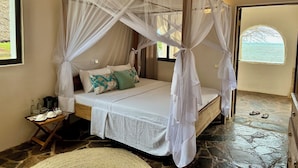 A room with a four-poster bed, a small table with a coffee maker, and a view of the sea through an arched window. - Mwazaro Beach Lodge (Shimoni)