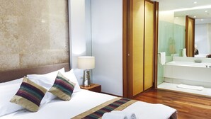 Ein Hotelzimmer mit einem großen Bett, einem Nachttisch mit Lampe, einem Holzschrank und einem Badezimmer mit Waschbecken und Spiegel.