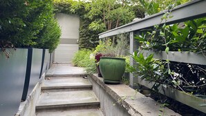 Eine schmale Betontreppe führt zu einem verschlossenen Bereich mit dichtem Grünwerk und einem großen, grünen Pflanzkübel auf der rechten Seite.