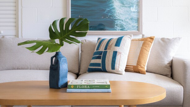 Una sala de estar con un sofá, una mesa de centro, un florero azul con una planta y dos libros.