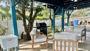 Un patio exterior con zona de estar techada, dispensador de agua y una parrilla.