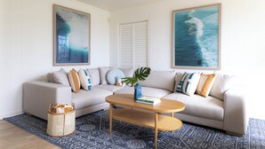 Una sala de estar con un sofá modular, una mesa de centro, una planta y dos grandes obras de arte mural que representan escenas marinas.
