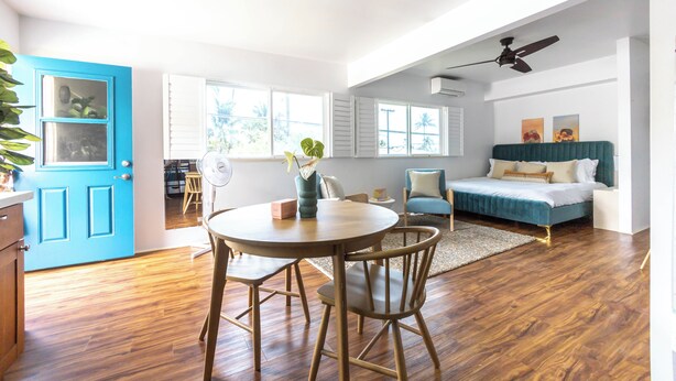 Ein geräumiges Zimmer mit Holzboden, einem runden Esstisch, einem blauen Sofa und einem Deckenventilator.