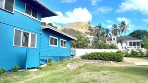 Ein zweistöckiges blaues Haus mit Vorgarten, im Hintergrund ein Berg und ein klarer Himmel.