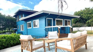 Ein blaues Haus mit Veranda, Holzmöbeln und einem gemusterten Teppich.