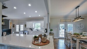 A spacious kitchen with a large island, white cabinets, and a dining area with wooden chairs and a table. - Bama Farmhouse - Beautiful Pool Area! (Tuscaloosa)