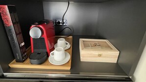 Una kitchenette compacta con una cafetera, una caja de cápsulas Nespresso, dos tazas blancas y una caja de madera con el nombre "Tea".