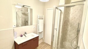 Un baño con ducha de vidrio, un lavamanos blanco con espejo y un perchero para toallas.