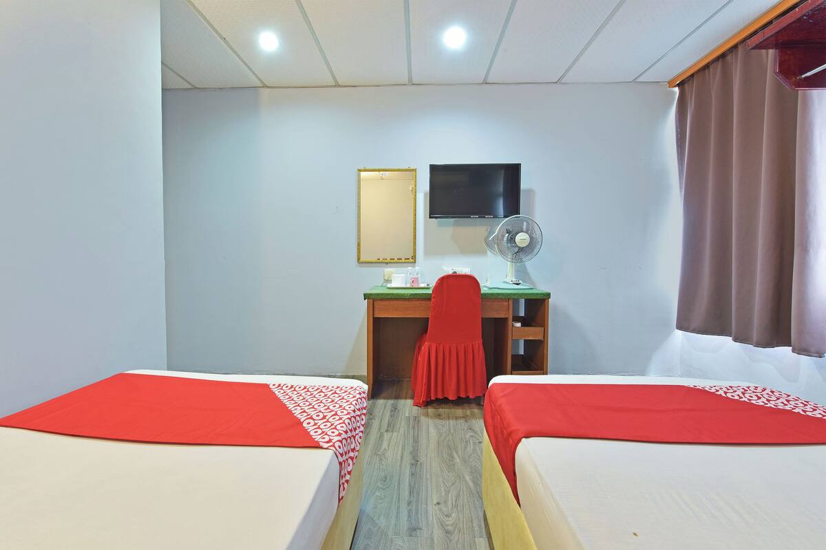 A room with two beds, a desk, a chair, a mirror, a TV, and a fan.