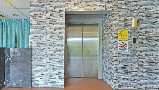 An elevator with a stone wall, a no smoking sign, and a phone on the wall. - OYO 90846 Hotel Akasia (Sungai Petani)