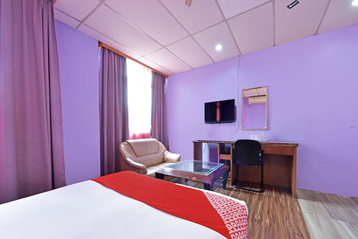 A hotel room with a bed, a desk, a chair, a television, and a window with curtains.