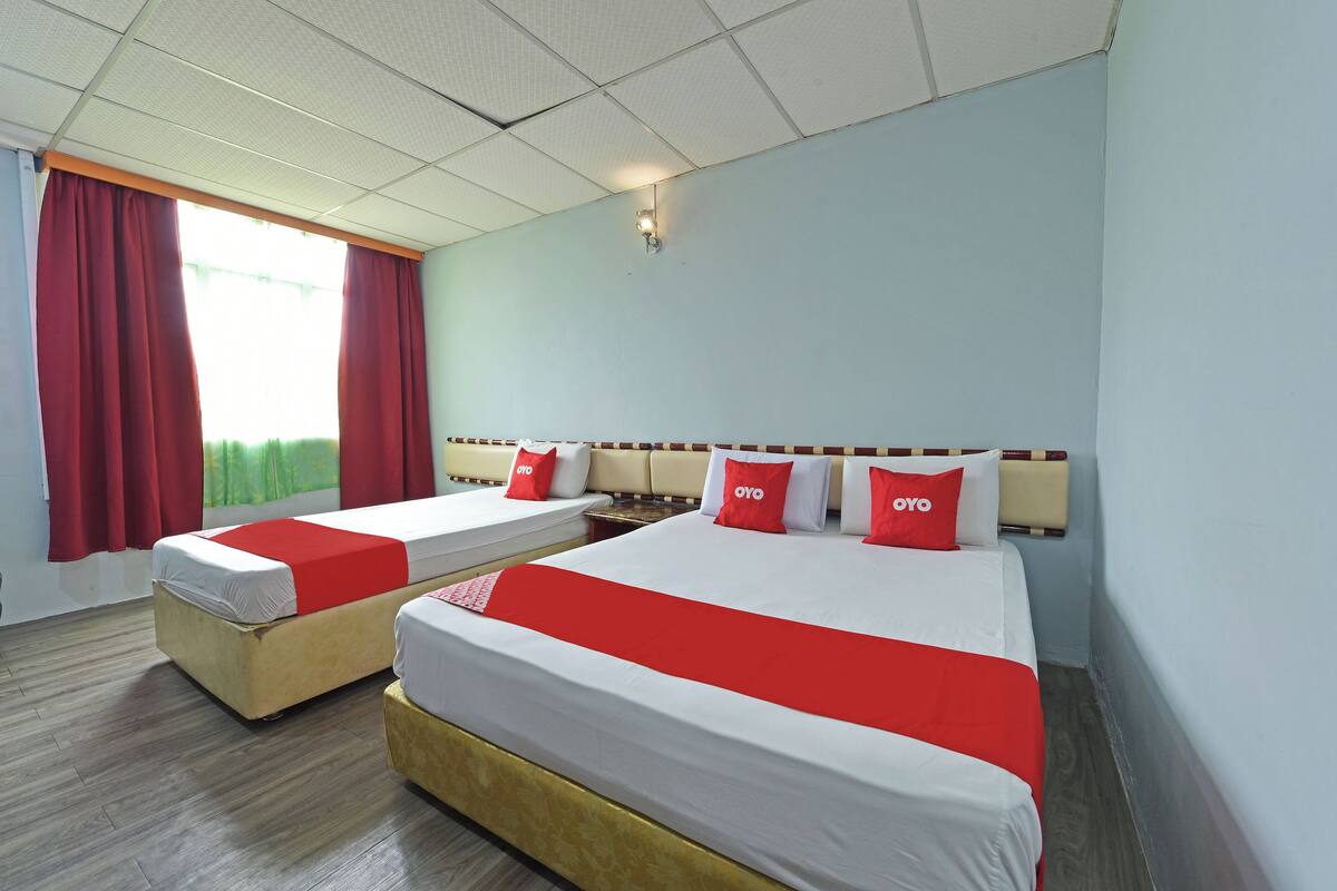 A hotel room with two beds, red and white bedding, a wooden floor, and a window with red curtains.
