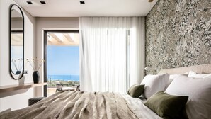 Ein Schlafzimmer mit einem großen Bett, Meerblick, einer Wand mit Muster und einem Fenster mit durchsichtigen Vorhängen.