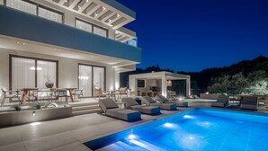 Ein modernes, zweistöckiges Haus mit Schwimmbecken, Außenbereich mit Sitzgelegenheiten und einer überdachten Terrasse.