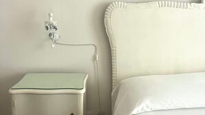 A bedroom with a white bed, a white nightstand with a lamp, and a wall-mounted branch. - Olga's House  (Otranto)
