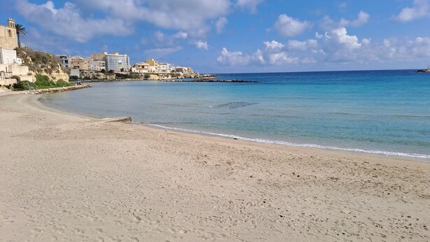 A sandy beach with footprints, a clear blue sky, and buildings in the background. - Olga's House  (Otranto)