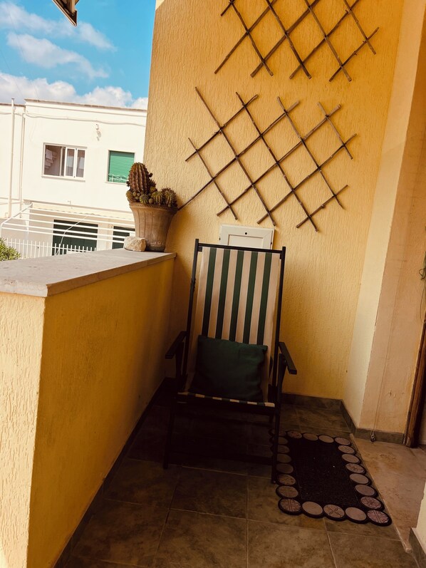 Un balcón con una silla, una planta en maceta y un panel decorativo en la pared.