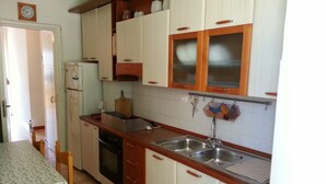 A compact kitchen with white cabinets, a wooden countertop, a sink, and a dining table with chairs. - Olga's House  (Otranto)