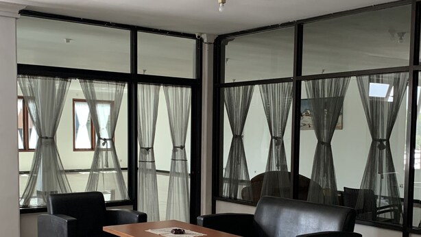 A modern living room with a sofa, two armchairs, a coffee table, and large windows with sheer curtains. - Hotel O Guest House Pandita (Tideng Pale)