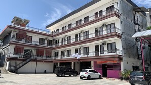A multi-story building with balconies, a staircase, and a parking area with cars. - Hotel O Guest House Pandita (Tideng Pale)
