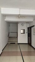 Um corredor com relógio, porta e escada que leva a outro cômodo.