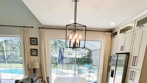 A modern kitchen with a large island, white cabinetry, and a view of a backyard with a pool. - Movie & Game rooms/Car Charger/Pool (Kissimee)