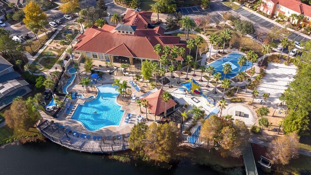 An aerial view of a resort with a swimming pool, palm trees, and a red-roofed building. - Movie & Game rooms/Car Charger/Pool (Kissimee)