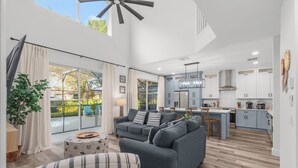 A modern living room with a grey sofa, a striped armchair, and a dining area with a kitchen in the background. - Movie & Game rooms/Car Charger/Pool (Kissimee)