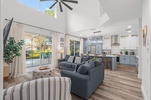 A modern living room with a grey sofa, a striped armchair, and a dining area with a kitchen in the background.