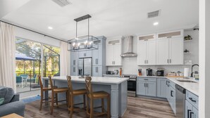 A modern kitchen with grey cabinets, a central island, and a dining area with wooden chairs. - Movie & Game rooms/Car Charger/Pool (Kissimee)